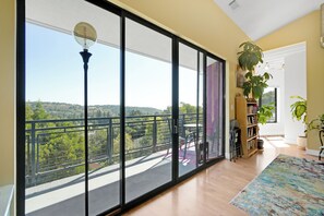 Een ruime kamer met een grote schuifglazen deur die uitkomt op een balkon met uitzicht op groen en heuvels.