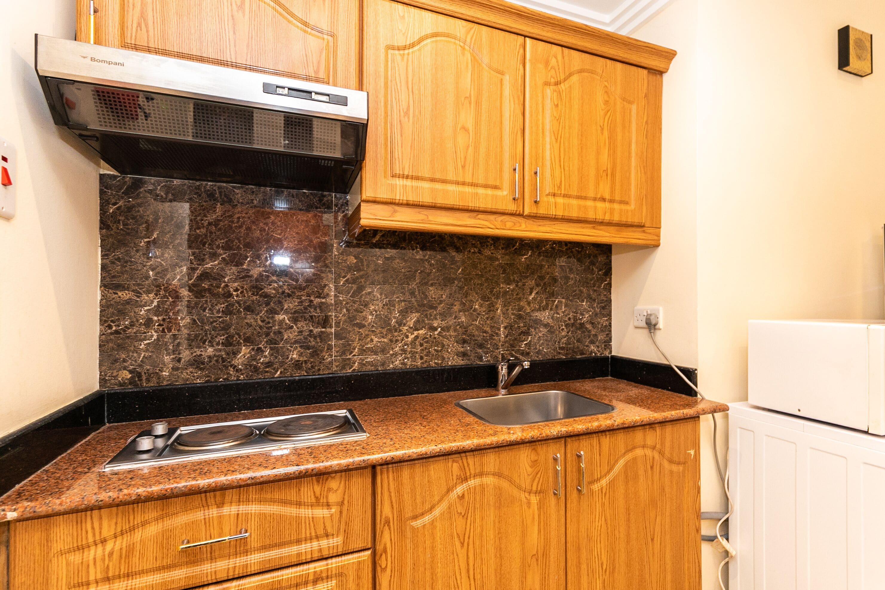A kitchen with wooden cabinets, a granite countertop, a stainless steel sink, and a built-in range hood.