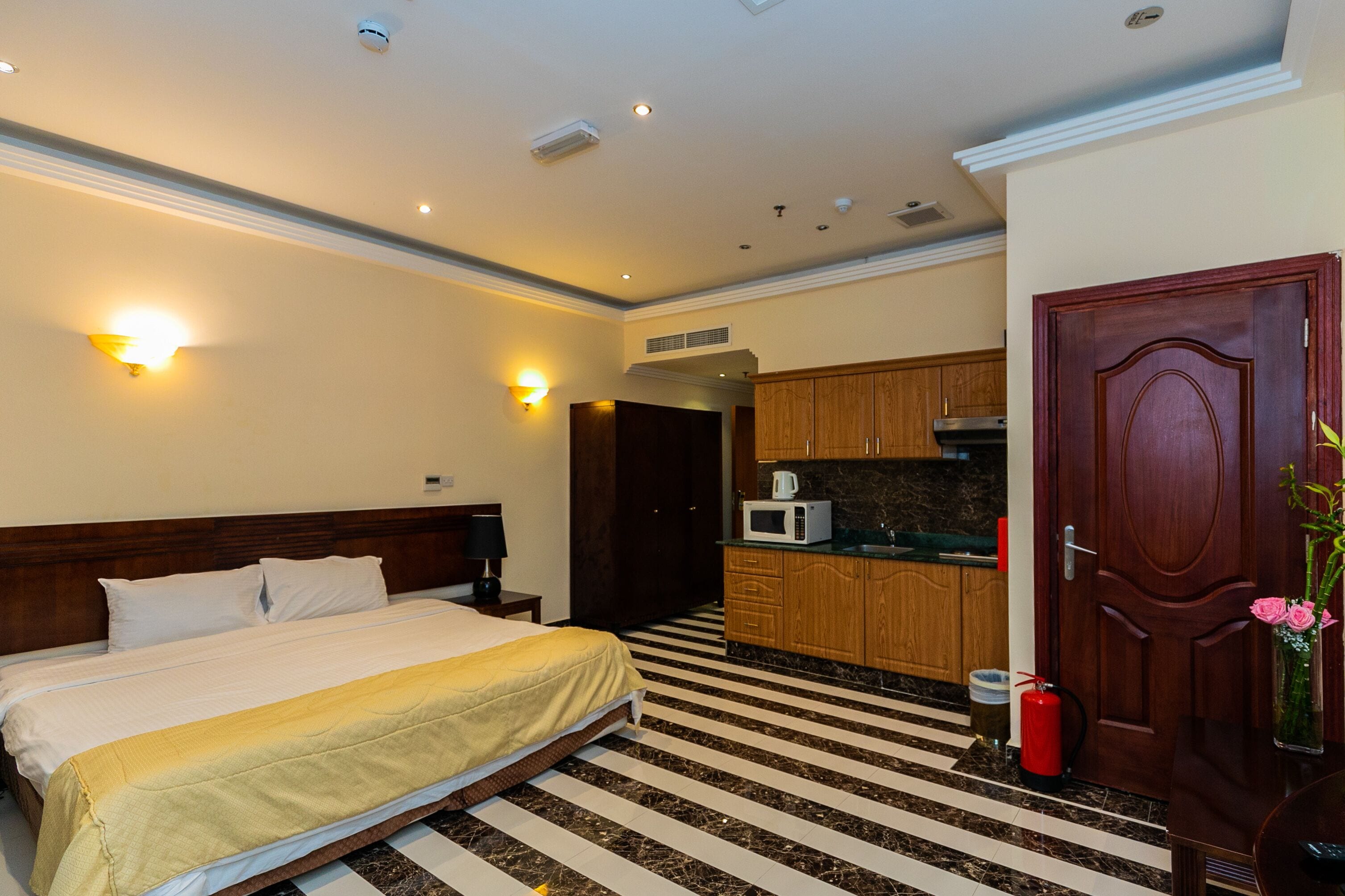 A hotel room with a bed, a nightstand, a microwave, a wooden cabinet, and a door.