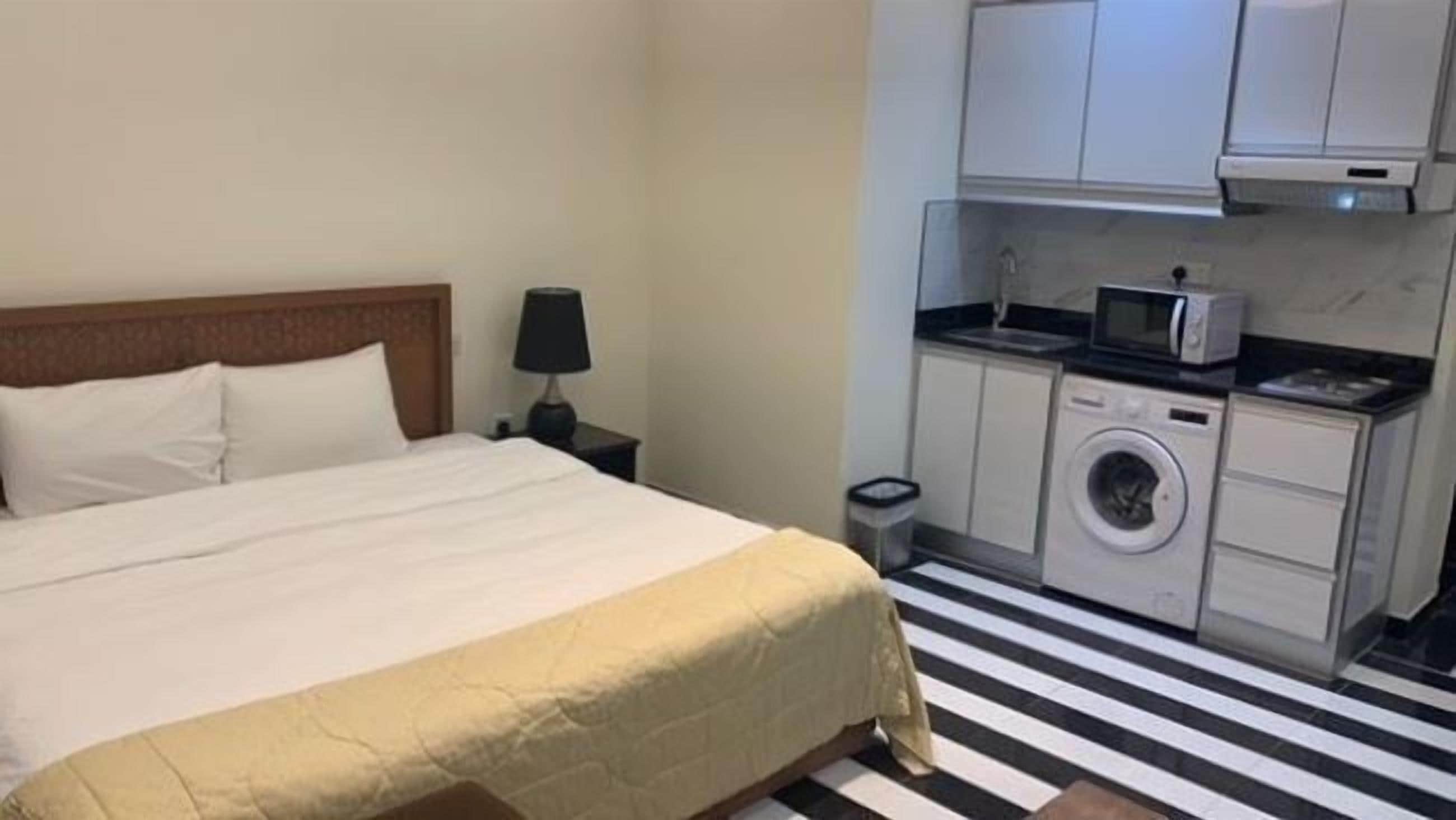 A hotel room with a bed, a nightstand, a lamp, a washing machine, and a microwave.