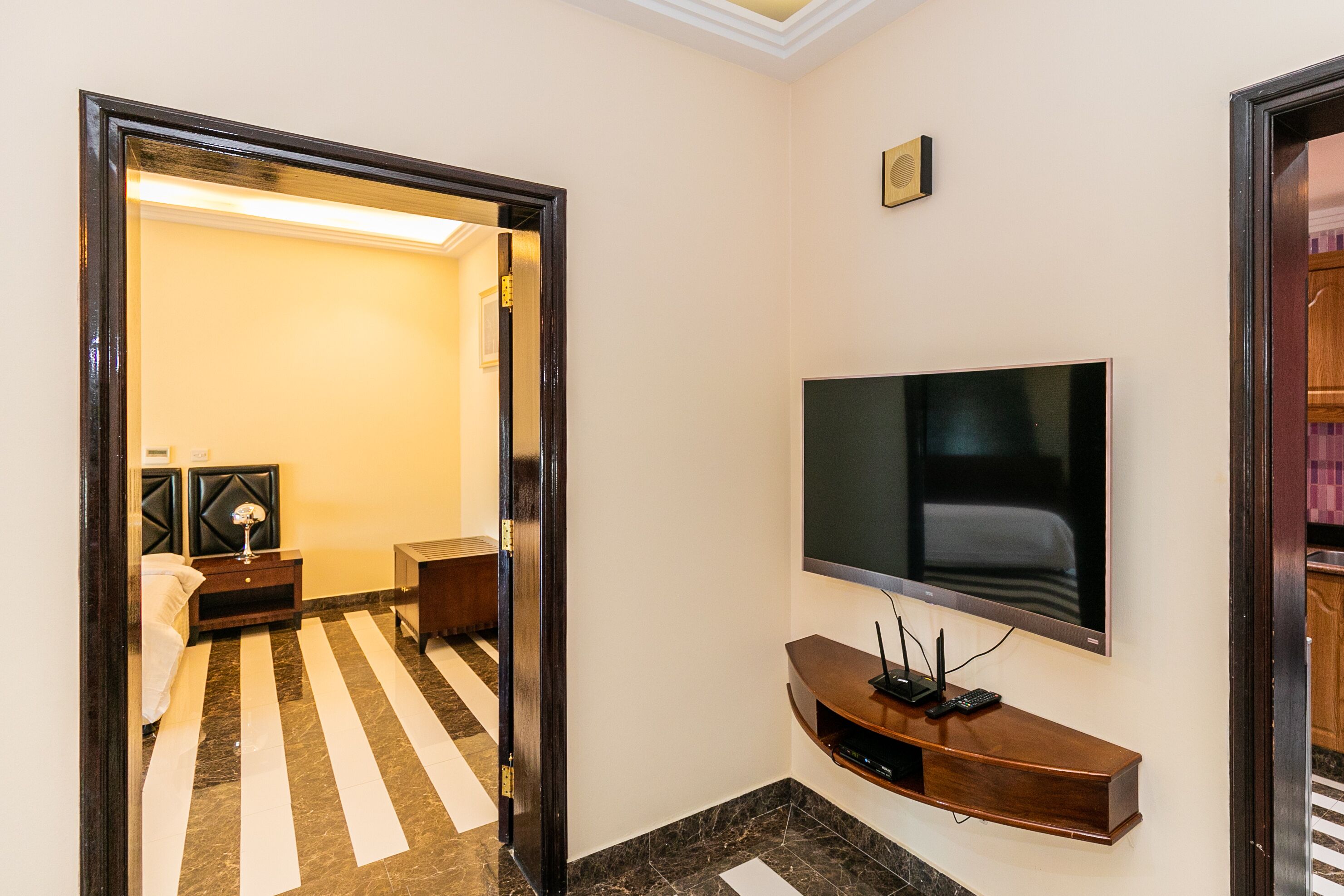 A hotel room with a large flat-screen TV mounted on the wall, a wooden console table below it, and a striped floor.