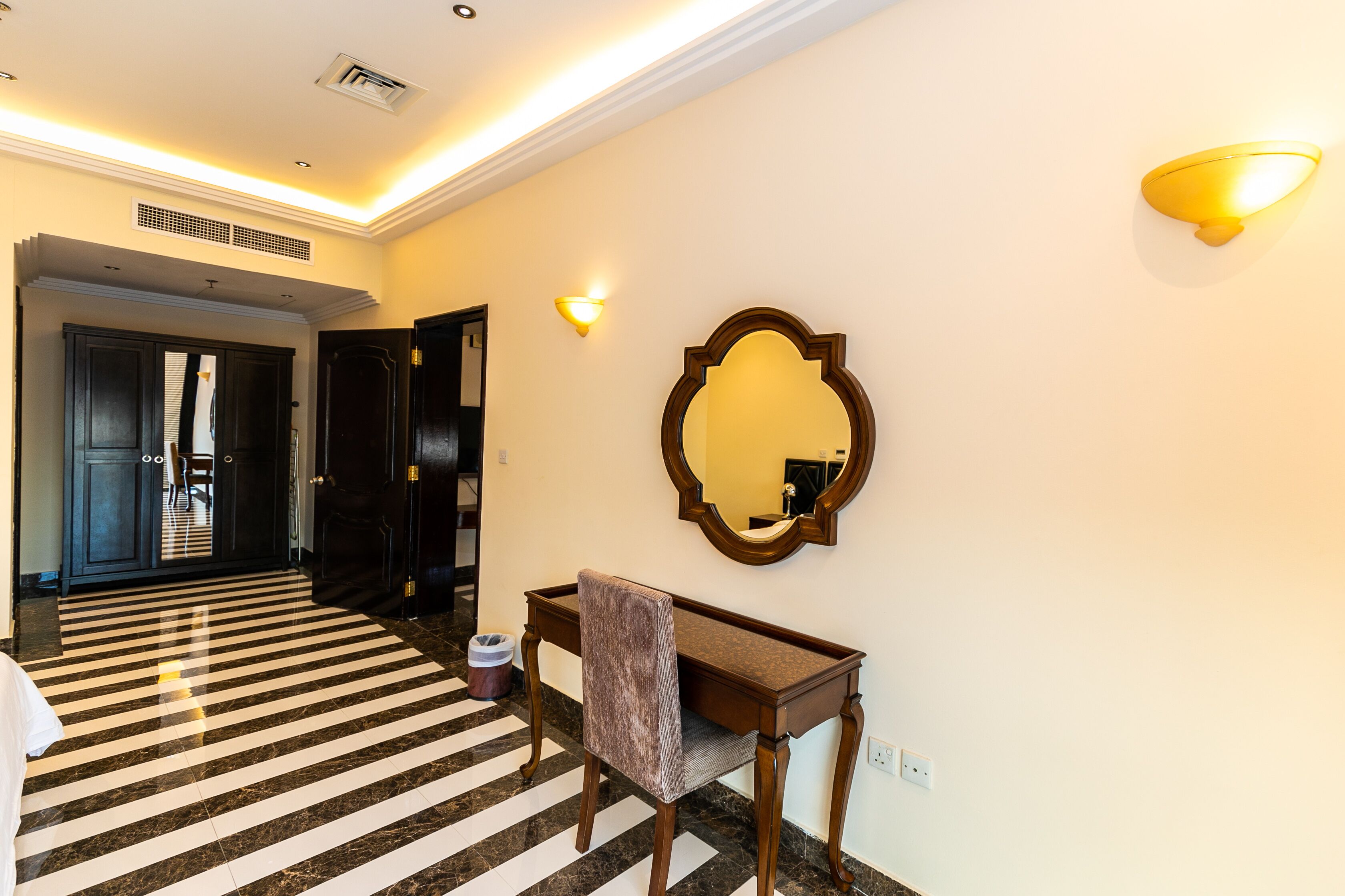 Vestíbulo de hotel con suelo a cuadros, mostrador con una silla, espejo montado en la pared y lámpara.