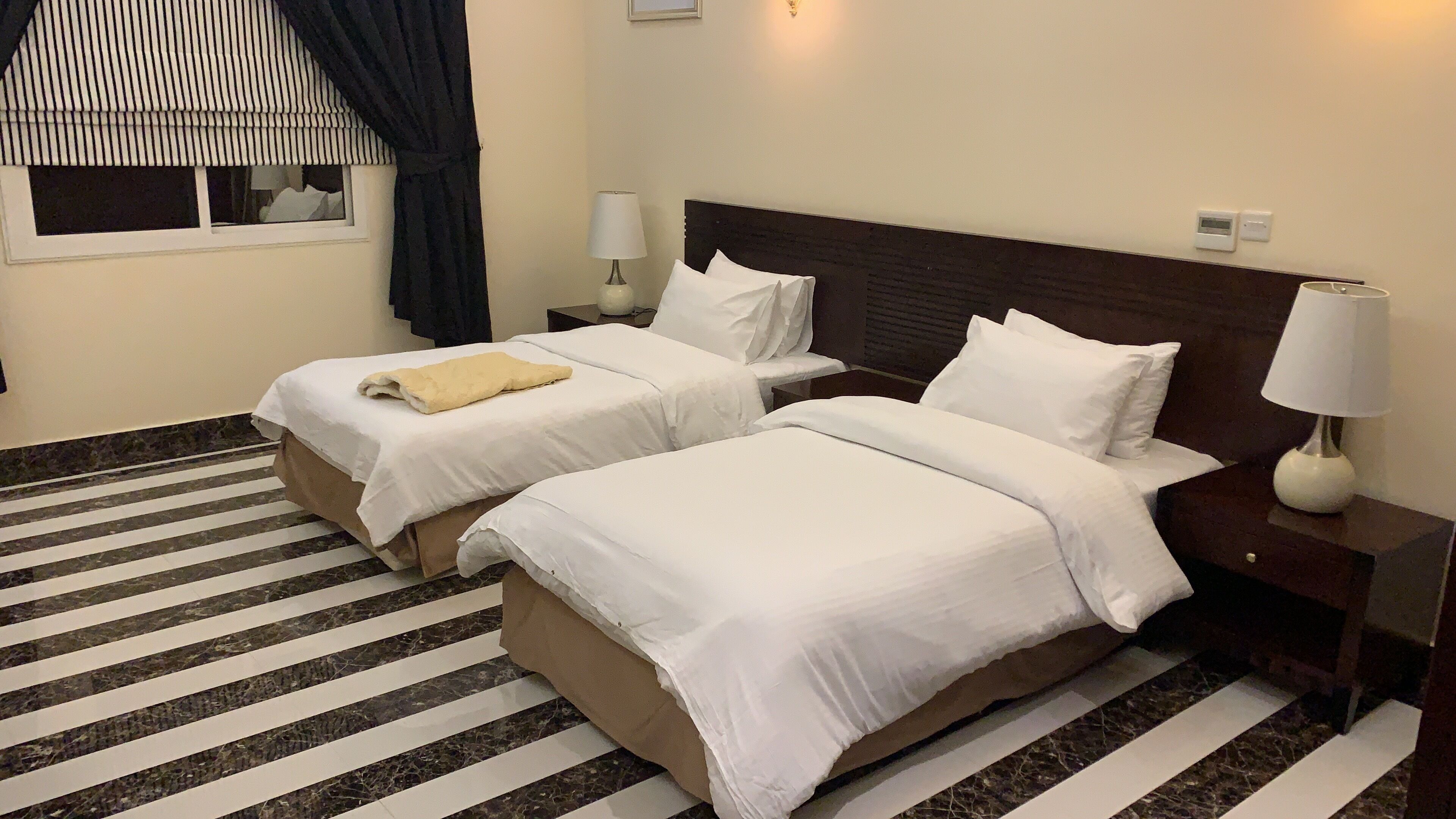 A hotel room with two beds, a striped rug, and a window with curtains.