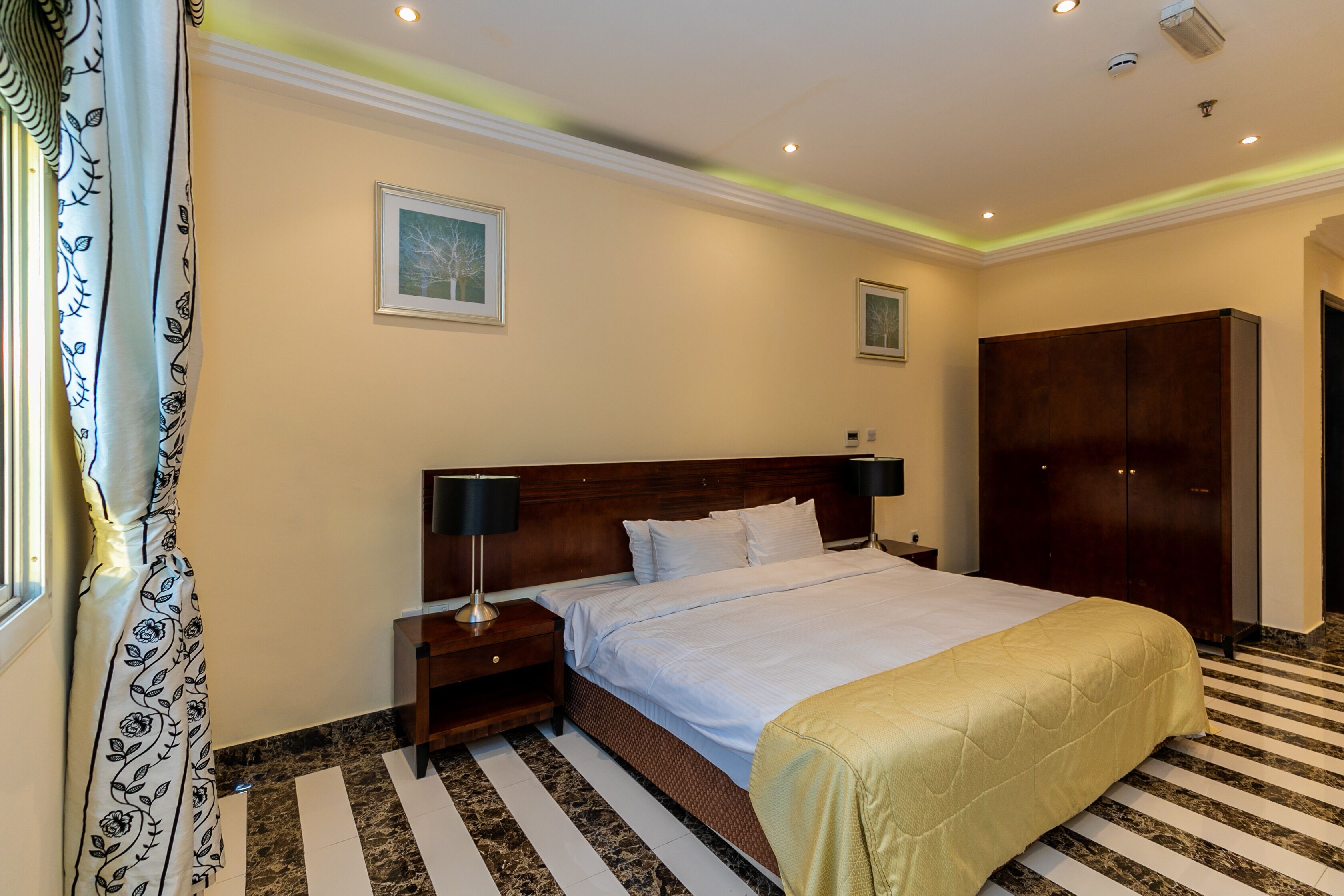 A hotel room with a large bed, a nightstand, a wardrobe, and a framed picture on the wall.