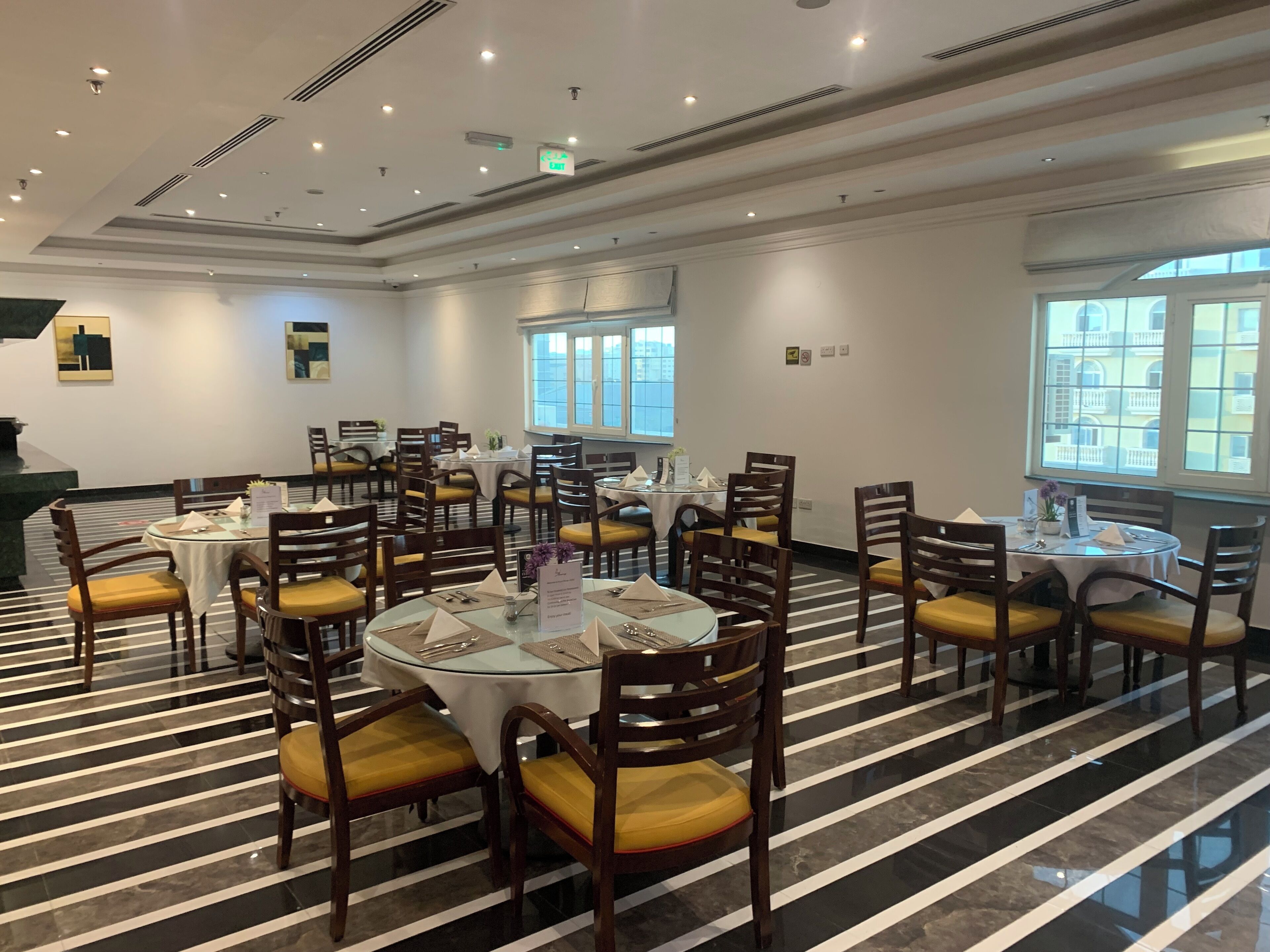 Un vaste espace dédié à la salle à manger, avec des tables et des chaises rondes, un sol à rayures et de grandes fenêtres offrant une vue sur la ville.