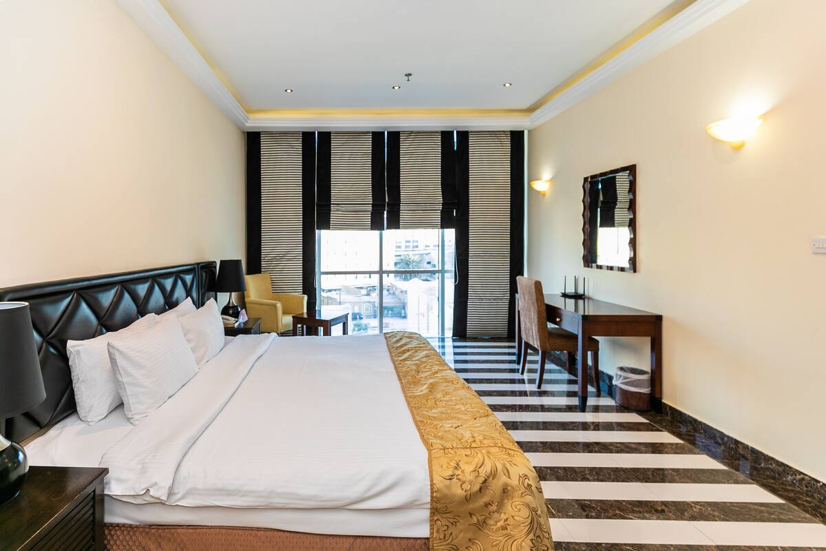 Une chambre d’hôtel avec un grand lit, un bureau, une chaise et une fenêtre avec des stores.