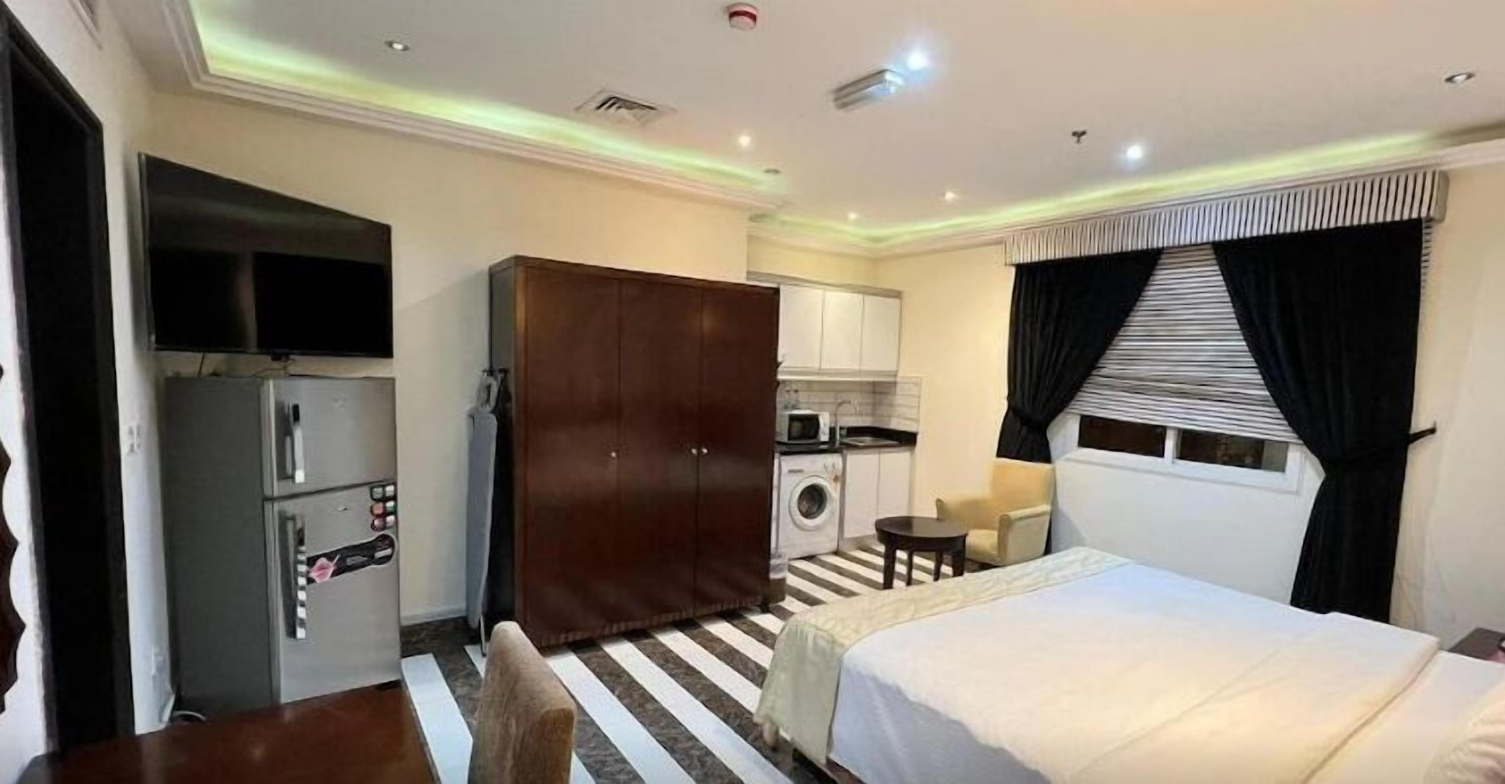 A hotel room with a bed, a desk, a wardrobe, a washing machine, and a television.
