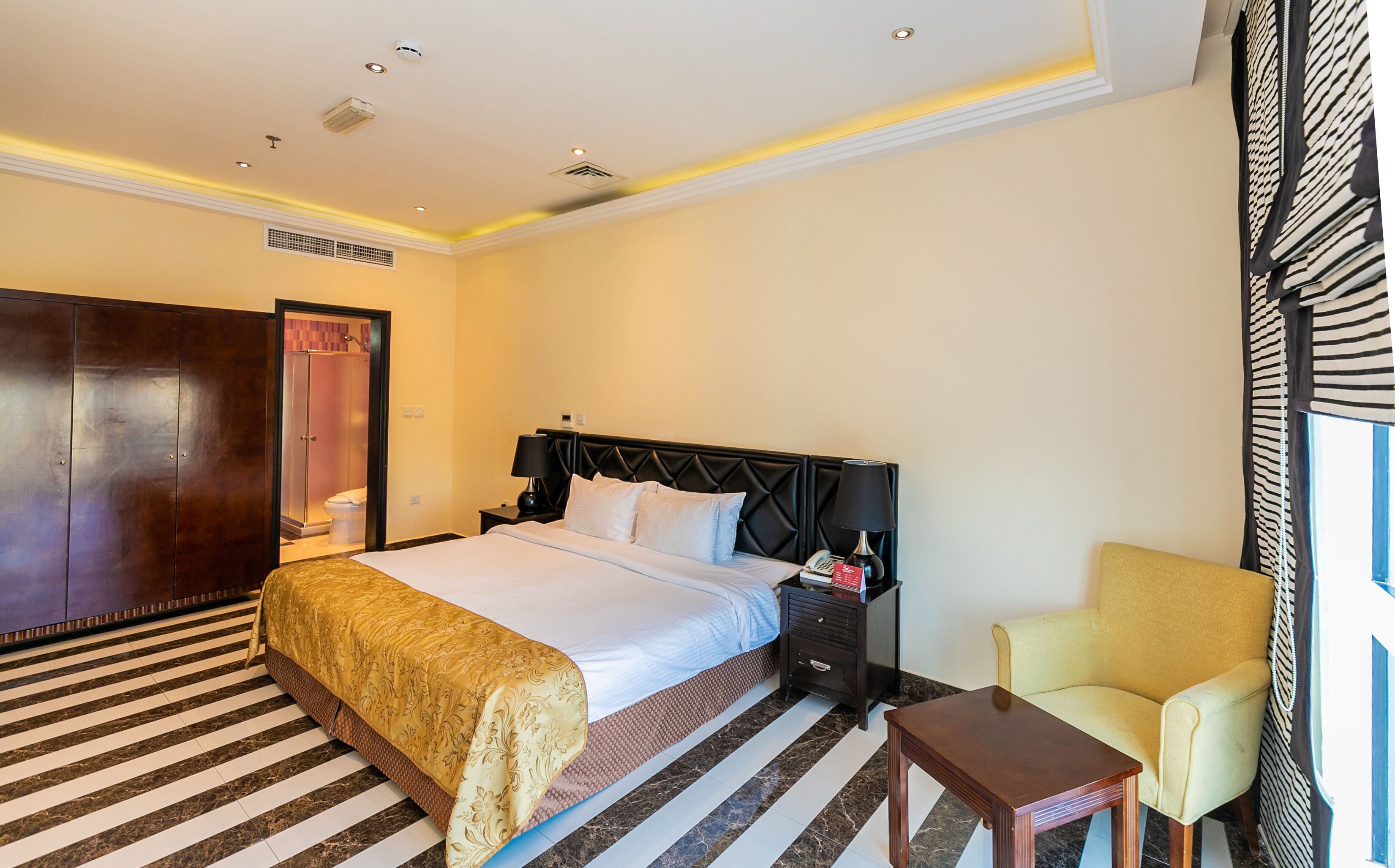 A hotel room with a bed, a nightstand, a chair, a wardrobe, and a shower.
