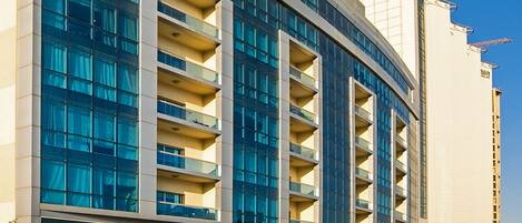 Un hotel moderno con varios balcones, ventanas amplias y una señalización destacada que indica una ubicación.