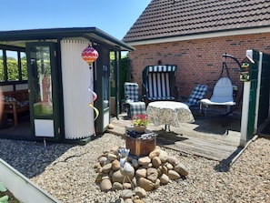 A covered outdoor seating area with a table and chairs, a hot air balloon decoration, and a small garden with rocks and a planter. - Ferienwohnung Am Schoolpad, 95152 - Ferienwohnung Am Schoolpad (Rhauderfehn)