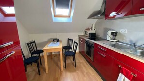 A compact kitchen with a dining table, chairs, a microwave, a coffee maker, and a red cabinet.