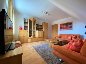 Een woonkamer met een bank, een salontafel, een televisie en een houten kast met glazen deuren.