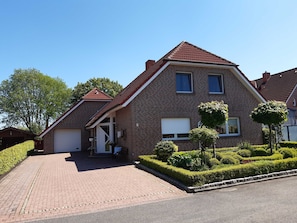 A two-story house with a brick exterior, a tiled roof, and a paved driveway. - Ferienwohnung Am Schoolpad, 95152 - Ferienwohnung Am Schoolpad (Rhauderfehn)