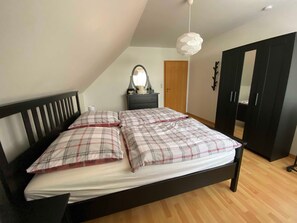 Een slaapkamer met een bed, een dressoir, een spiegel en een kledingkast.