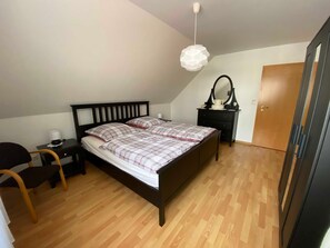Een slaapkamer met een bed, nachtkastje, stoel, kapstok en hanglamp.