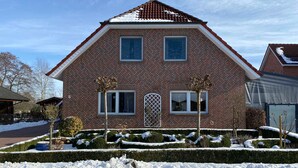 A two-story brick house with a symmetrical facade, a central entrance, and a snow-covered garden.