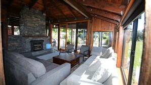A cozy living room with a stone fireplace, large windows, and a wooden ceiling.