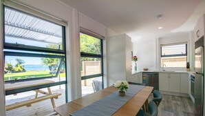 A modern kitchen with white cabinets, a stainless steel refrigerator, and a window overlooking a deck.