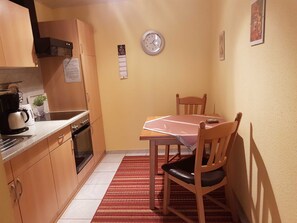 Une cuisine de taille réduite, avec des meubles en bois, une machine à café et une horloge au mur.