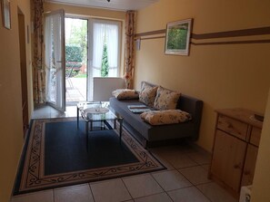 Un salon comprenant un canapé, une table basse en verre, un tapis à motifs, un radiateur et un meuble en bois.