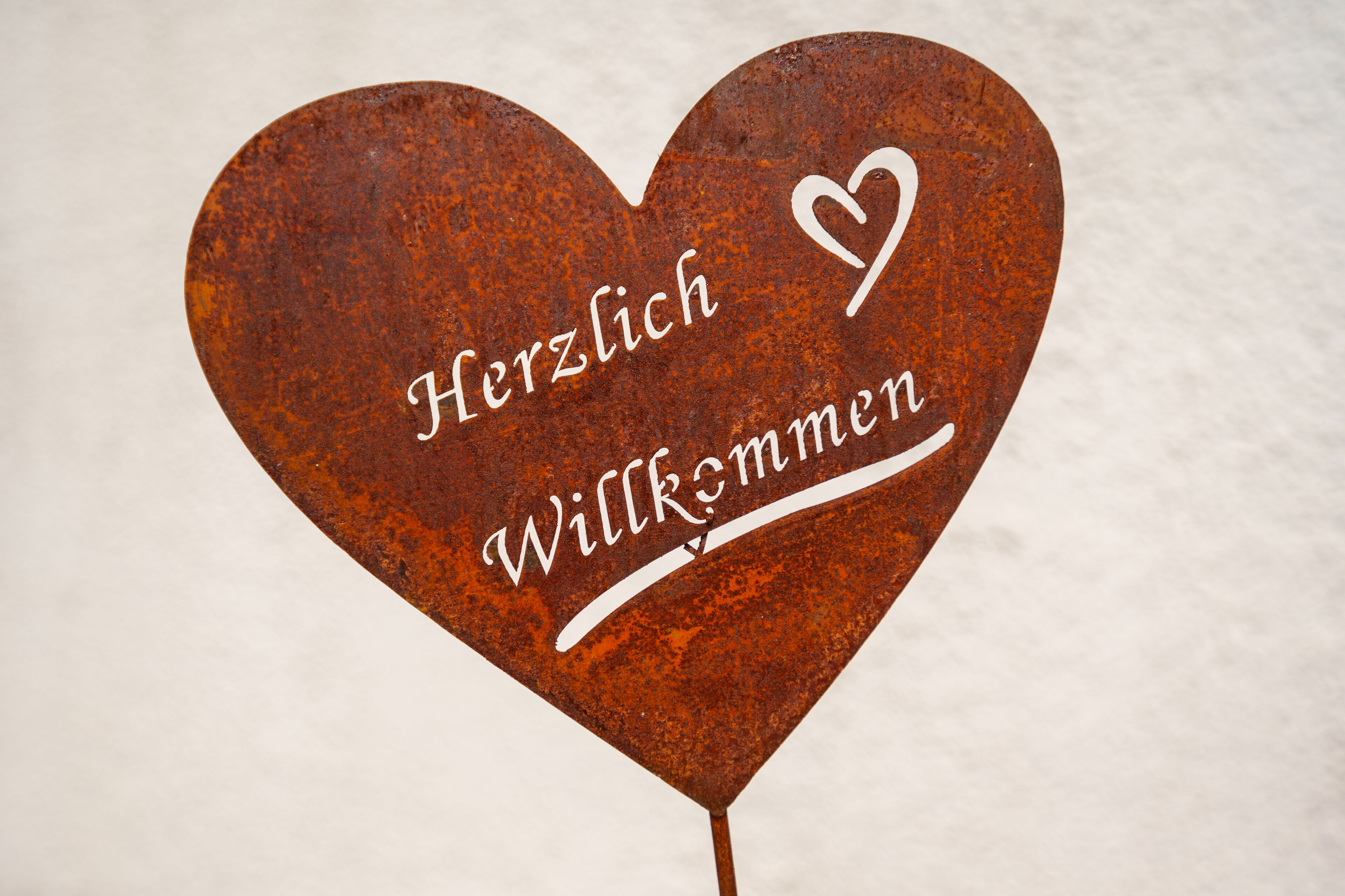 Un letrero con forma de corazón que dice 'Herzlich Willkommen' (Bienvenido) en letras blancas.