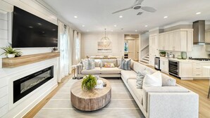 A modern living room with a fireplace, a large TV, a round coffee table, and a sofa. - Amour La Mer by AvantStay | Rooftop Patio, Pool Access, Walk to Beach (Seacrest)