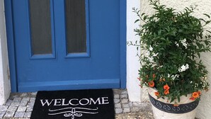 A blue door with a 'WELCOME' mat and a potted plant with flowers. - Urlaub im Wunderschönen Hegau mit Alpenblick (Tengen)