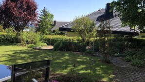 A garden with a paved area, a metal chair, and a building with a tiled roof in the background. - Urlaub im Wunderschönen Hegau mit Alpenblick (Tengen)