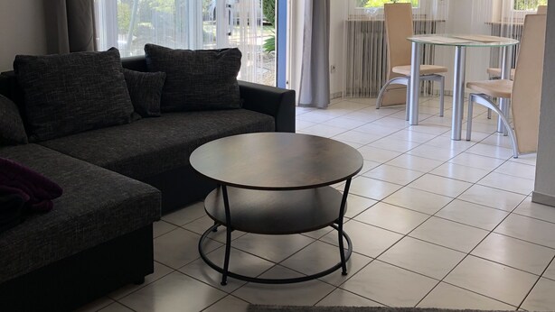 A modern living room with a sectional sofa, a round coffee table, and a dining area with chairs and a table. - Urlaub im Wunderschönen Hegau mit Alpenblick (Tengen)