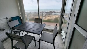 A balcony with a table and chairs, overlooking a beach and rocky shoreline.