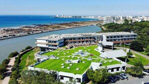 A coastal hotel with a rooftop garden, a marina, and a view of the sea and cityscape.