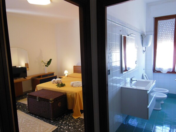 A hotel room with a bed, bedside table, lamp, and a small wooden chest.