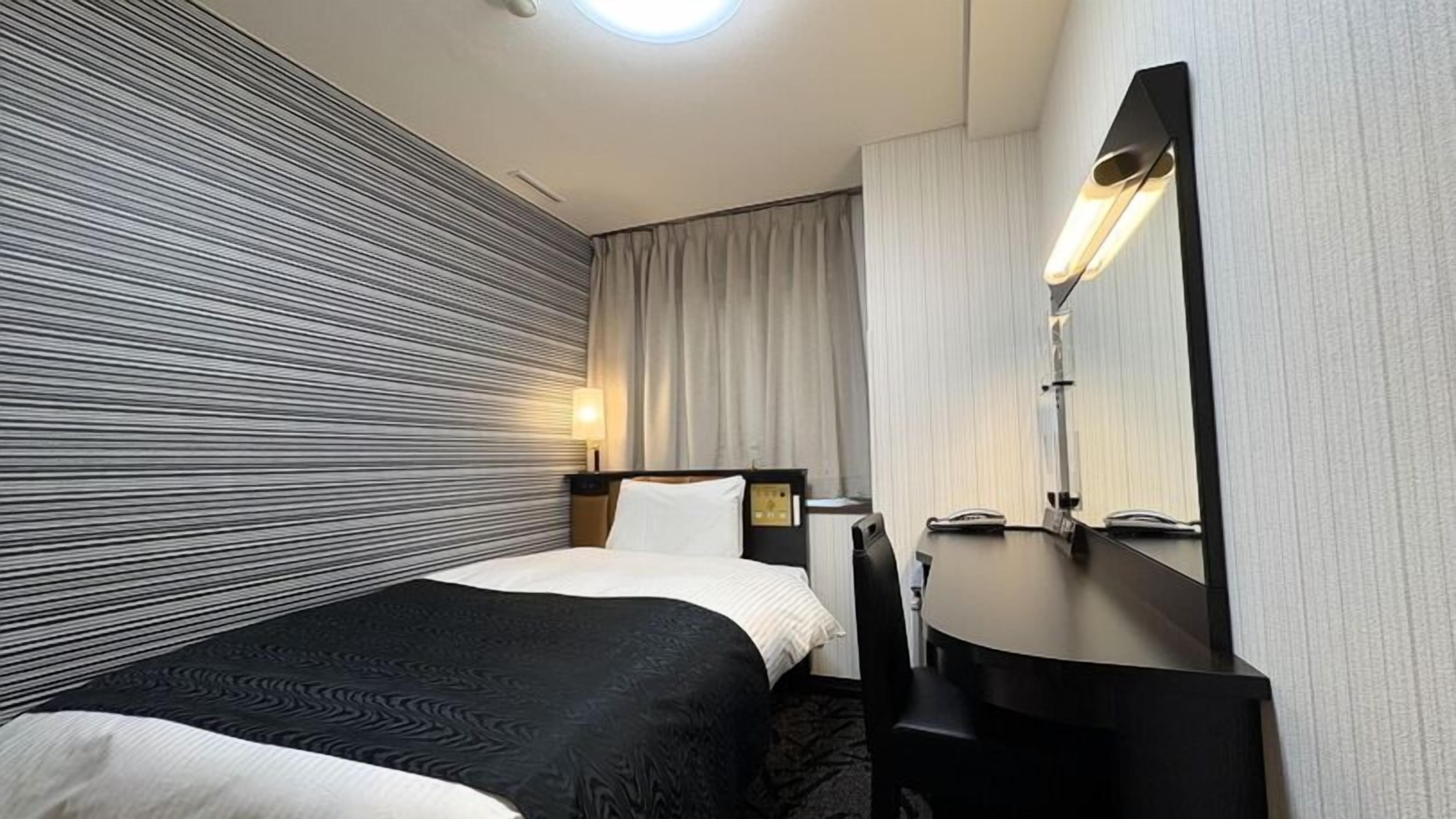 Een hotelkamer met een bed, een bureau, een stoel, een lamp en een spiegel.