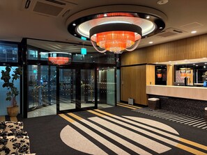 Un hall d’hôtel doté d’une porte tournante, d’un comptoir d’accueil et d’un grand lustre.