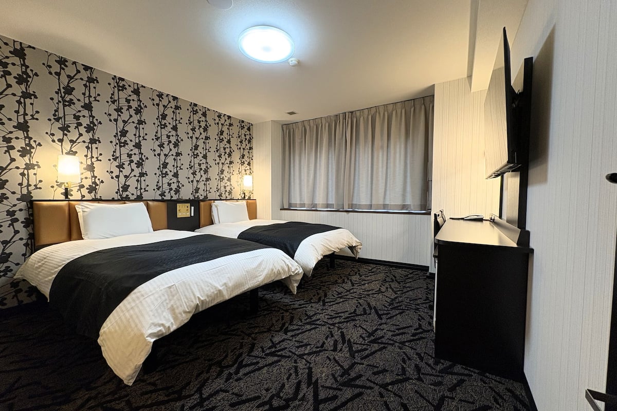 Habitación de hotel con dos camas, un espejo grande, televisor de pantalla plana y una ventana con cortinas.