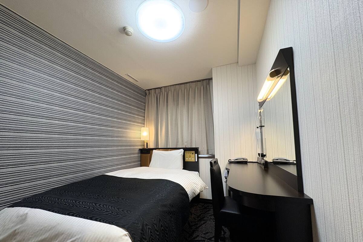 Una habitación de hotel con cama, mesita de noche, lámpara y espejo.