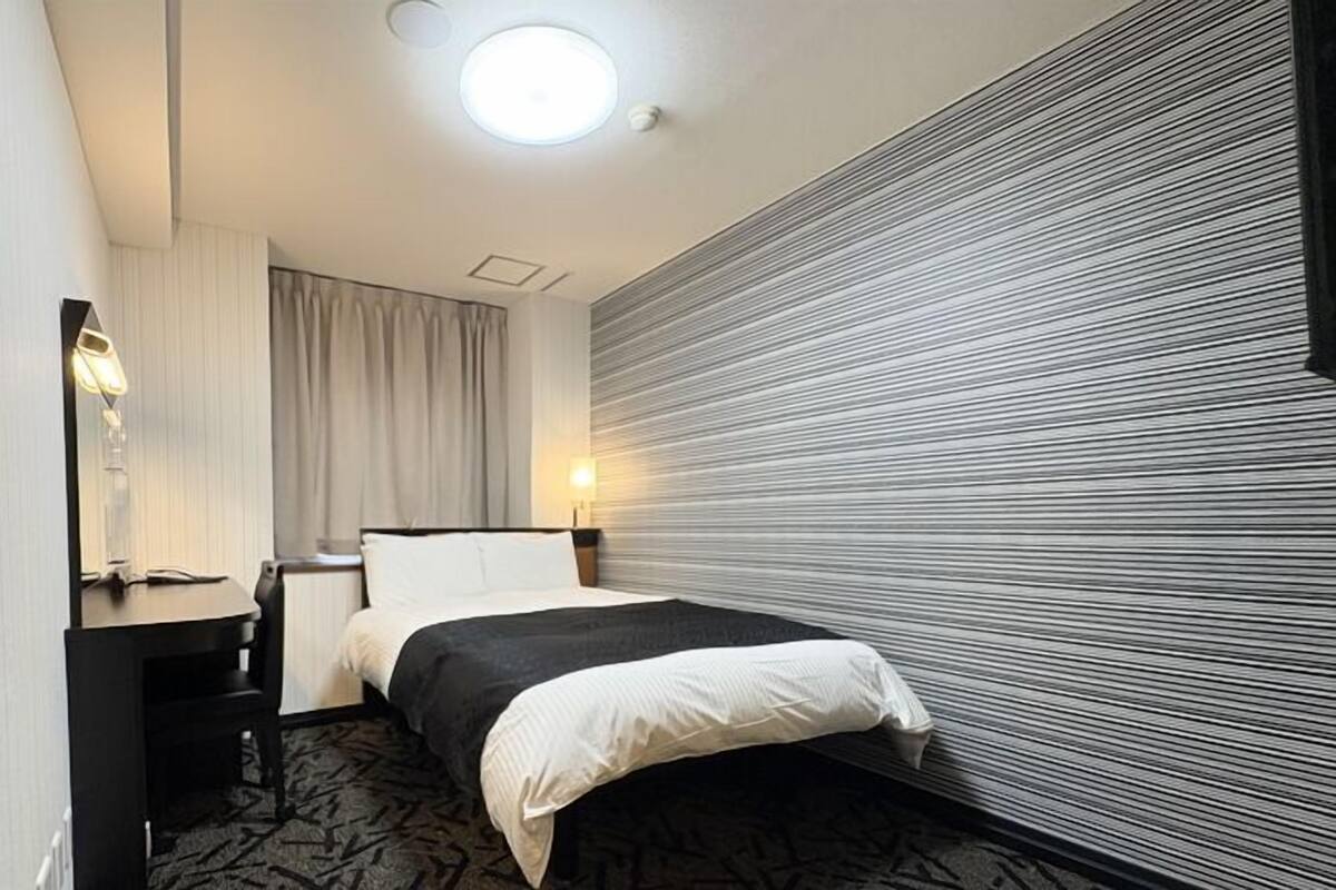 Una habitación de hotel con una cama, un escritorio, un espejo y una pared con textura.