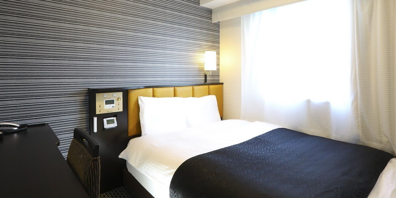Une chambre d’hôtel avec un lit, un bureau, un panneau de commande et une fenêtre avec des rideaux.