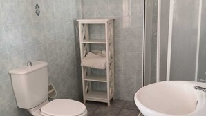 A bathroom with a toilet, bidet, sink, and a small shelf unit. - Residence Terrazza Vendicari (noto)
