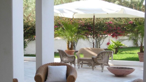 An outdoor patio with wicker furniture, a white umbrella, and potted plants. - Residence Terrazza Vendicari (noto)