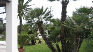 A well-maintained garden with palm trees and a white building structure. - Residence Terrazza Vendicari (noto)
