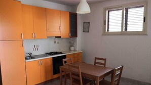 A kitchen with orange cabinets, a white countertop, a stove, and a dining table with chairs. - Residence Terrazza Vendicari (noto)