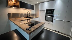 A modern kitchen with a central island, built-in oven, and stainless steel appliances. - Petite Maison (Le Lavandou)