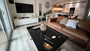 A modern living room with a leather sofa, a black coffee table, and a TV mounted on the wall. - Petite Maison (Le Lavandou)