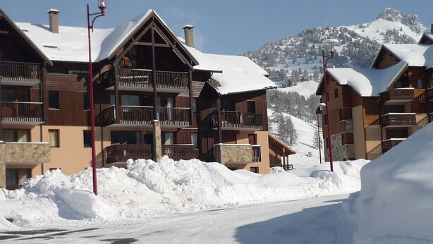 Una località montana innevata con edifici in legno, balconi e cielo sereno.