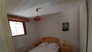 Una camera da letto con un letto singolo, una testiera in legno, comodini con lampade, una finestra con stipite in legno e una ventola a soffitto.