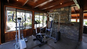 A gym with exercise equipment, large windows, and a stone wall. - Fantail Brand New Absolute Lakefront Whole House (Rotorua)