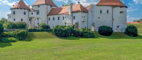 A large, historic building with multiple towers and a well-maintained lawn in front.