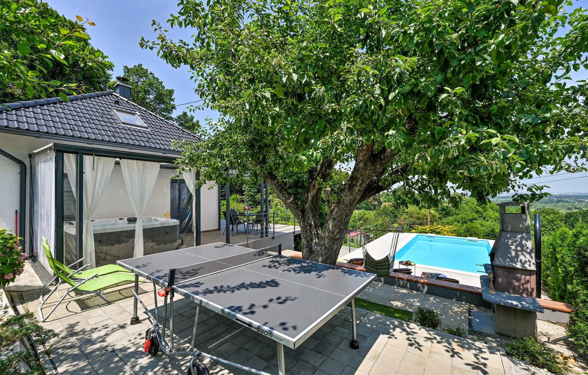 Un espacio exterior techado con mesa de ping pong, jacuzzi y piscina.