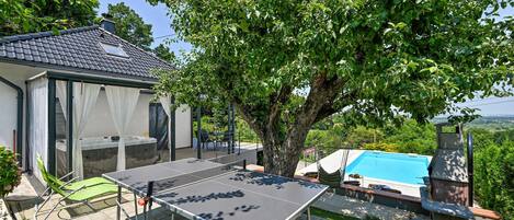 Un espacio exterior techado con mesa de ping pong, jacuzzi y piscina.